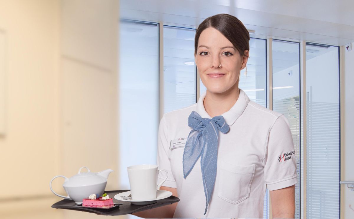 Hotel employee with afternoon tea and pastries on a tray, smiling into the camera